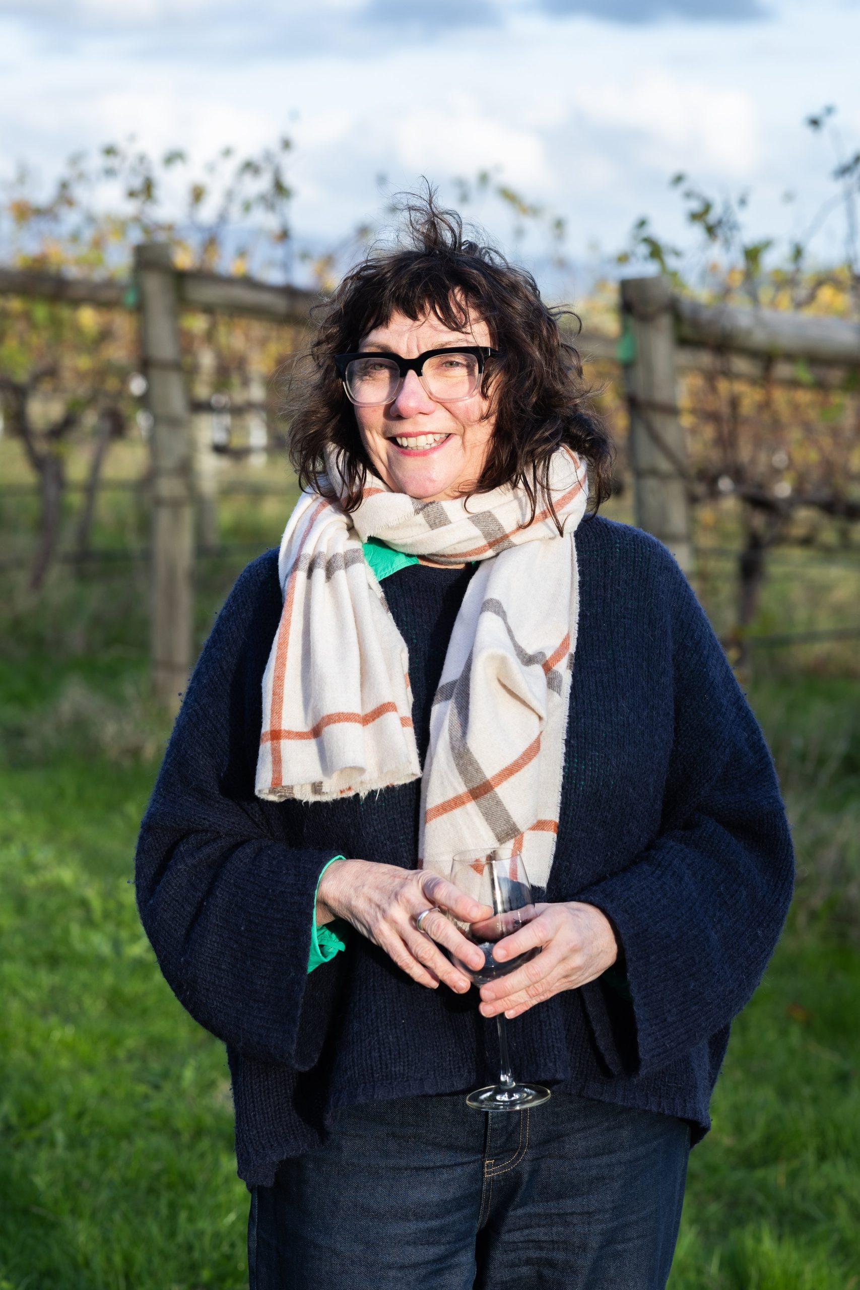 We are a full service media agency, specialising in the hospitality and lifestyle industries. We create content and foster connection and collaboration. The photo is of Hilary McNevin standing in a vineyard. She is holding a glass of red wine and wearing a particularly attractive checked scarf.